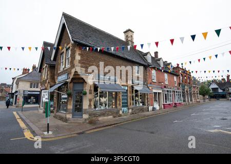 Eine ruhige Straßenszene auf dem Marktplatz von Oakham, die steinerne Ladenfronten zeigt, die an einem bewölkten Tag mit bunten festlichen Fahnen geschmückt sind. Stockfoto
