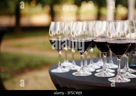 Eine Nahaufnahme einer Reihe eleganter Rotweingläser auf einem drapierten schwarzen Tisch bei einer Veranstaltung im Freien, perfekt für Hochzeits-, Bankett- und Empfangsthemen, Premium-Cateringservice, anspruchsvolle Tischgestaltung Stockfoto