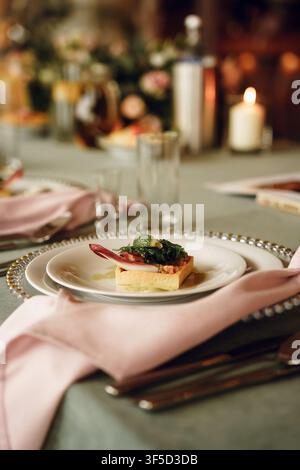 Ein eleganter Vorspeisen auf einem feinen Esstisch serviert mit einer rosa Serviette und sanftem Kerzenlicht, raffinierte festliche Atmosphäre, Luxus-Restaurant-Catering, besonderes Event-Gourmet und romantisches Gala-Dinner Stockfoto