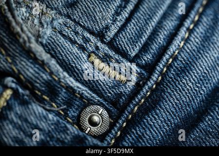 Detail von blauem Jeansstoff, das Textur, Nähte und Metallknopf-Niete zeigt Stockfoto