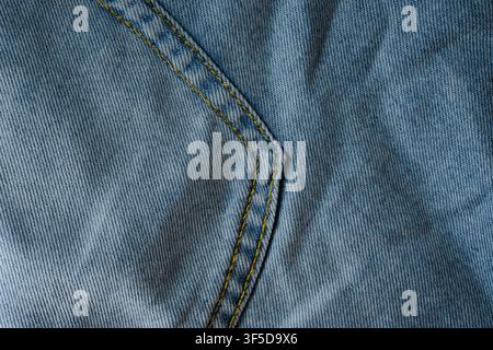 Blaues Denimgewebe mit einer Naht mit gelben Stichen und diagonaler Textur Stockfoto