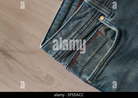 Blaue Denimjeans zeigen die Stofftextur mit Tasche und orangefarbenen Nähdetails auf Holz Stockfoto