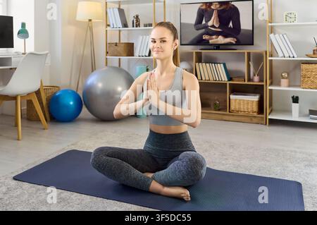 Junge Frau praktiziert Yoga zu Hause, Online-Meditationskurs im Fernsehen Stockfoto