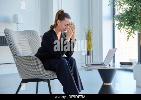 Gestresste Geschäftsfrau, die mit Arbeit überfordert ist und den Kopf in den Händen hält, in der Nähe eines Laptops Stockfoto