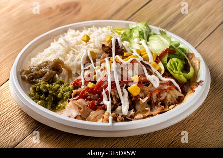 Hühnershawarma-Teller serviert mit Basmatireis, frischem Salat, gegrilltem Hühnchen, Gemüse und cremiger Knoblauchsauce, fotografiert auf einem Holztisch Stockfoto