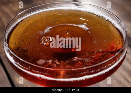 Nahaufnahme eines Tropfens auf einem Whiskey Manhattan, serviert auf einem rustikalen Holzuntergrund Stockfoto