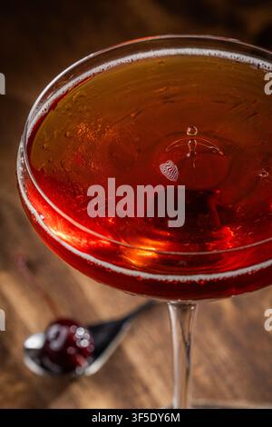 Nahaufnahme eines Tropfens auf einem Whiskey Manhattan, serviert auf einem rustikalen Holzuntergrund Stockfoto