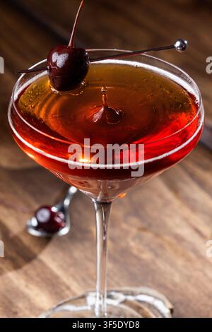 Nahaufnahme eines Tropfens auf einem Whiskey Manhattan, serviert auf einem rustikalen Holzuntergrund Stockfoto