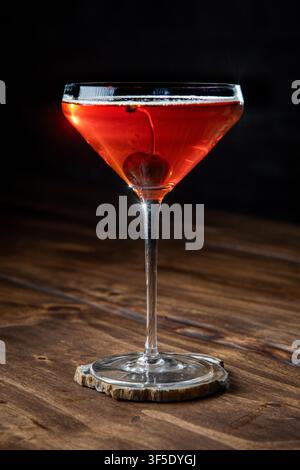 Nahaufnahme eines Whiskey Manhattan, serviert mit einer Kirsche auf einem rustikalen Holzgrund Stockfoto