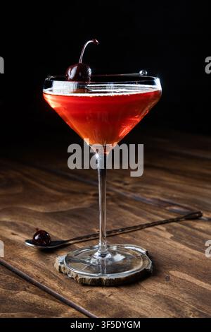 Nahaufnahme eines Whiskey Manhattan, serviert mit einer Kirsche auf einem rustikalen Holzgrund Stockfoto