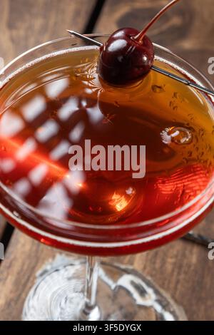 Nahaufnahme eines Whiskey Manhattan, serviert mit einer Kirsche auf einem rustikalen Holzgrund Stockfoto