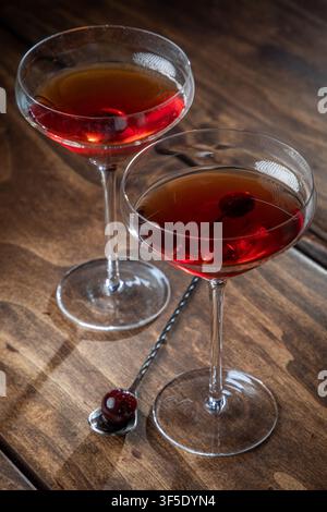 Zwei Whiskey-Manhattans serviert mit einer Kirsche auf einem rustikalen Holzgrund Stockfoto