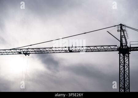 Niedrigwinklige Silhouette eines schweren Turmdrehkrans vor einem stimmungsvollen, wolkigen grauen Himmel, der städtische Entwicklung, Ingenieurwesen und moderne Infrastruktur repräsentiert Stockfoto