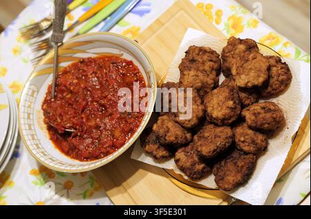 Gebratene Fleischbällchen, die auf Küchenpapier ruhen und überschüssiges Öl absorbieren, serviert mit einem schmackhaften hausgemachten Tomatendip in einer kleinen Schüssel, wodurch ein köstlicher Snack entsteht Stockfoto