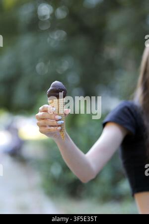 Frauenhand hält ein erfrischendes schokoladengetränktes Eis in einer Waffel und genießt einen süßen Sommerschmaus im Freien mit stilvoll lackierten Fingernägeln Stockfoto