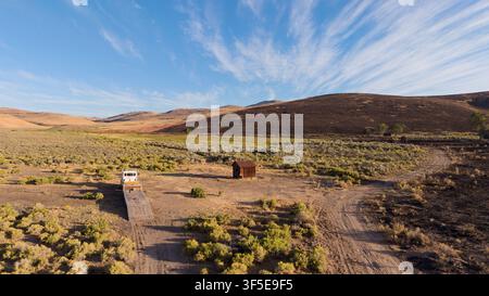 Verlassene Linienhütte und Tieflader-Truck im Salbeibusch, Lassen County, Kalifornien; Biscar-Feuer-Brandmuster und rote Feuerschutzfärbung am Hang. Stockfoto