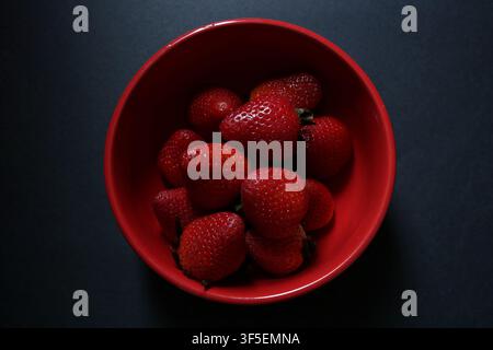 Frische rote Erdbeeren in einer roten Schale auf einem dunklen Hintergrund Stockfoto