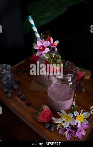 Erdbeer- und Blaubeer-Smoothies in Mason-Gläsern mit Blumen- und Frucht-Dekor Stockfoto