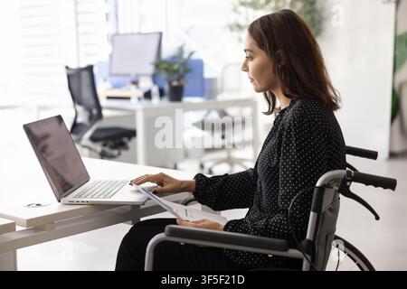 Konzentrierte Geschäftsfrau im Rollstuhl, die an einem Laptop arbeitet Stockfoto