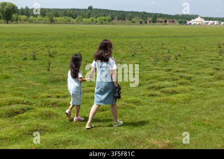 Die Rückseiten von zwei asiatischen Mädchen, die DSLR-Kameras tragen und auf dem Grasland gehen Stockfoto