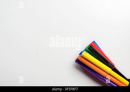 Ein Bündel lebendiger, mehrfarbiger Filzstifte, die in der Ecke einer sauberen weißen Oberfläche angeordnet sind und reichlich Platz für Text lassen. Ideal für pädagogische a Stockfoto