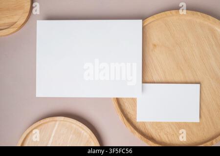 Leere weiße leere Gruß- oder Einladungskarte, Namenskarte, Holzplatte auf beigem Hintergrund. Mock-up-Präsentation. Minimaler moderner Stil mit Kopierraum Stockfoto