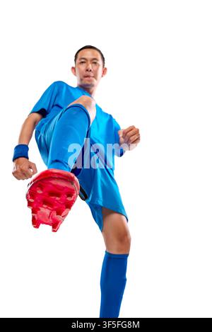 Vollständige Studioaufnahme eines entschlossenen indonesischen südostasiatischen Fußballspielers in einem blauen Trikot und roten Stollen, in einer dynamischen Pose vor einem Stockfoto