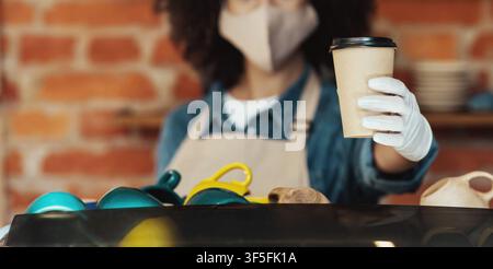 Mitarbeiter im Café bietet Getränke zum Mitnehmen an, sicheres Restaurant mit Lieferservice Stockfoto