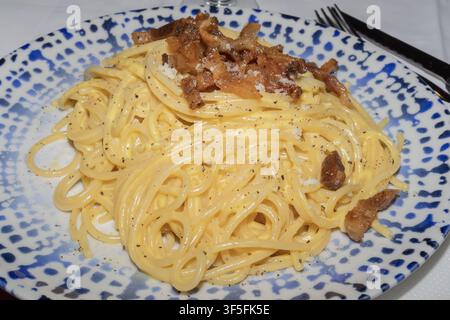 Traditionelle italienische Spaghetti Carbonara mit knusprigem Guanciale, cremiger Eier-Käse-Sauce, geriebenem Käse und schwarzem Pfeffer auf dem Teller serviert Stockfoto