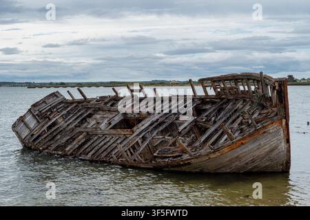 Rostiges Wrack liegt schräg in ruhigem Wasser unter wolkigem Himmel Stockfoto