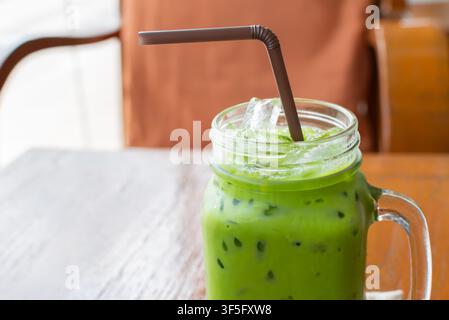 Erfrischendes Eismatcha-Latte, serviert in einer klaren Glastasse mit Eiswürfeln und Strohhalm auf Holztablett, perfekt für Café-Menü-Sommergetränke und gesunde Erfrischung Stockfoto