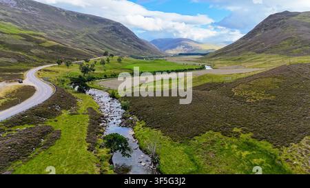 Luftaufnahme eines sich windenden Hochlandbaches, der durch ein Tal fließt, umgeben von sanften Hügeln unter dramatischen Sommerhimmel in den schottischen Highlands Stockfoto