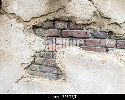 Verwitterte rissige Putzwand, die Ziegelsteinmauer freilegt Stockfoto