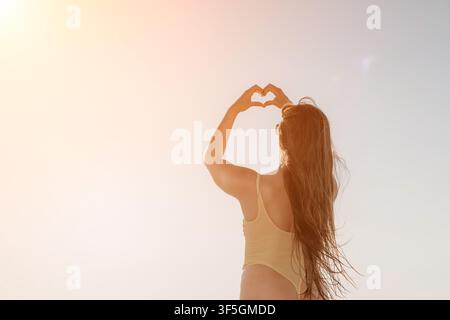 Herz-Hände-Frau steht unter der hellen Sommersonne und zeigt eine Liebessymbol-Geste mit Kopierraum Stockfoto