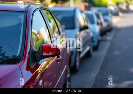 Rotes Auto und eine Reihe geparkter Fahrzeuge entlang einer ruhigen Straße mit Selektivität Stockfoto