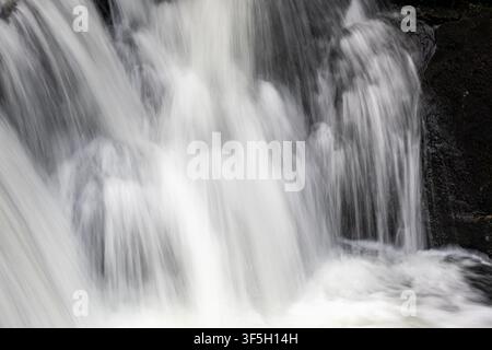 Nahaufnahme von kaskadierendem Wasser, das über dunkle Felsen an Rhaeadr Cymerau in Schwarzweiß fließt Stockfoto