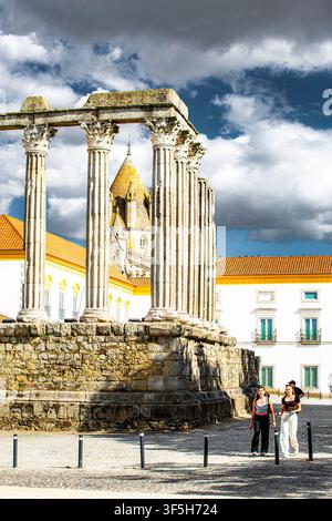 Antike römische Tempelruinen ragen in Évora, Portugal, empor. Steinsäulen erheben sich vor dramatisch bewölktem Himmel. Besucher erkunden die historische Stätte und halten fest Stockfoto