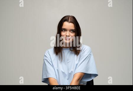 Junge Frau zeigt ein spielerisches Grinsen, schaut mit Neugier und nachdenklichen Augen in die Kamera Stockfoto