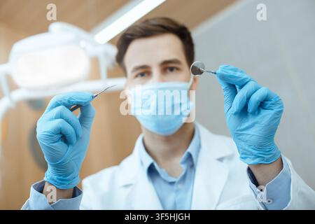 Millennial freundlich Stomatologe in weißem Mantel, Schutzmaske und Gummihandschuhe arbeiten mit professioneller Ausrüstung Stockfoto