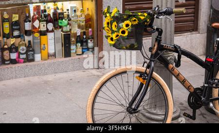 Fahrrad mit künstlichen Sonnenblumen in einem Drahtkorb, das an einem Pfosten vor einem Spirituosengeschäft in Porto, Portugal, angeschlossen ist — Konzept: Urbane Radkultur Stockfoto