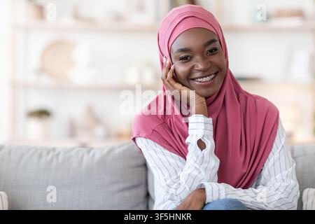 Modern Modesty. Lächelnde schwarze Frau in Hijab posiert auf dem Sofa zu Hause Stockfoto
