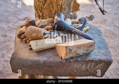 Eine Nahaufnahme zeigt eine Sammlung traditioneller handgeschnitzter Holzwerkzeuge und Klingen, die auf einem Steinblock in Damaraland, Namibia, ruhen. Stockfoto