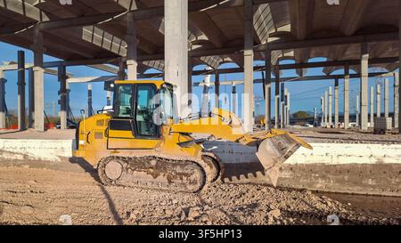 Gelber Raupenschlepper arbeitet auf einer großen Betonbaustelle. Schwere Industrieausrüstung. Stockfoto