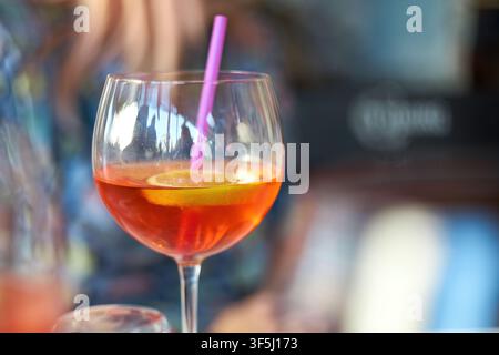 Nahaufnahme eines erfrischenden orangefarbenen alkoholischen Cocktails in einem großen Glaskelch, garniert mit einer schwimmenden Zitronenscheibe und einem rosa Strohhalm. Stockfoto