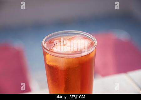 Nahaufnahme eines erfrischenden Orange-Spritz-Cocktails, gefüllt mit Eiswürfeln, serviert in einem klaren Glas auf einem hellen Tisch vor einem unscharfen Hintergrund. Stockfoto