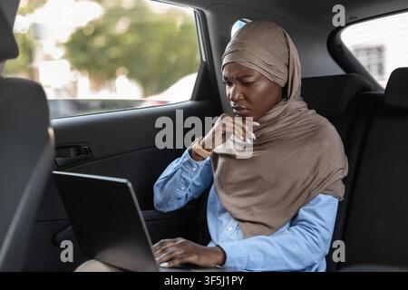 Betonte Black Islamic Geschäftsfrau Arbeiten Auf Laptop Auf Dem Rücksitz Von Auto Stockfoto