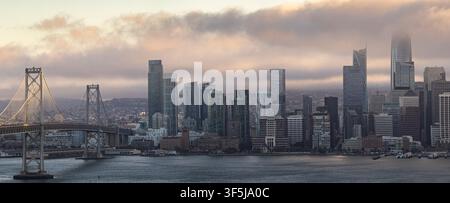 Panoramablick auf die Skyline von San Francisco und die Bay Bridge bei Sonnenaufgang, mit niedrigem Nebel und weichen Wolken über der Bucht, die ikonische Westküsten-Stadtlandschaft einfangen Stockfoto