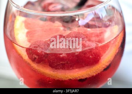 Nahaufnahme eines erfrischenden Pink-Gin-Cocktails, serviert in einem Glas mit frischen roten Himbeeren und einer Zitrusfrucht-Scheibe, die in dem Getränk schwimmt. Stockfoto