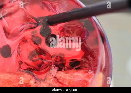 Eine Nahaufnahme eines erfrischenden Pink-Gin-Cocktails, garniert mit frischen Himbeeren, gemischten Beeren und Eiswürfeln in einem Glascup. Stockfoto