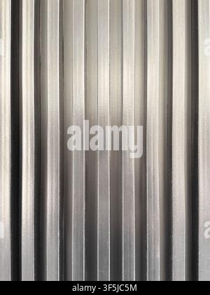 Nahaufnahme von vertikalen Wellblechplatten in Silber- und Grautönen, die eine abstrakte industrielle Textur mit sich wiederholenden Rillen, Schatten und Lin Stockfoto